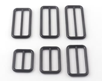 May include: Six black metal slider buckles of varying sizes. The buckles are rectangular with a single opening on each side.