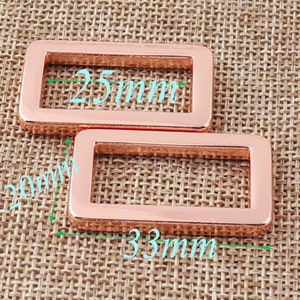 May include: Two rose gold metal rectangular rings with a smooth finish. The larger ring measures 33mm by 20mm and the smaller ring measures 25mm by 15mm.