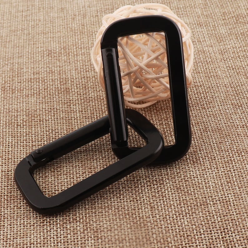 May include: Two black metal D-shaped carabiners linked together. The carabiners are made of a durable metal and have a smooth, polished finish.