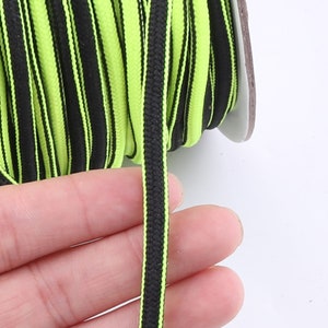 May include: A spool of black and neon green striped elastic cord. The cord is about 1/4 inch wide and is wound around a white spool.