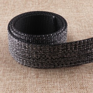 May include: Black woven webbing with a silver shimmer. The webbing is rolled up and has a textured surface.
