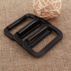 May include: Two black metal belt buckle slides. The slides are rectangular with a smooth, shiny finish.
