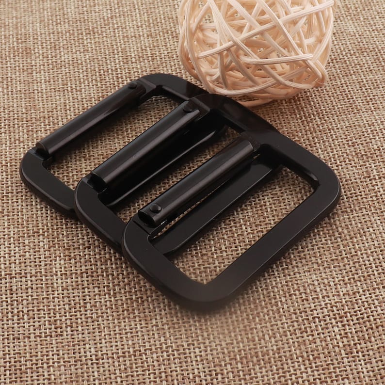 May include: Two black metal belt buckle slides. The slides are rectangular with a smooth, shiny finish.