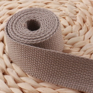 Puede incluir: Primer plano de una correa de tejido de algodón beige. La correa está enrollada y tiene una superficie texturizada.