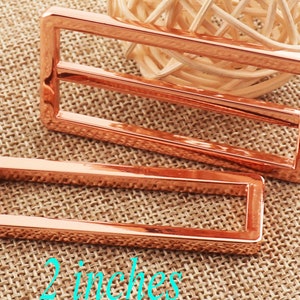 Puede incluir: Dos deslizadores de hebilla de cinturón de metal de color oro rosa. El deslizador más grande mide 5 cm de ancho y el más pequeño 2,5 cm de ancho.