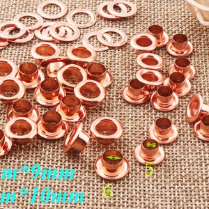 May include: A collection of rose gold eyelets in various sizes, including 5mm, 6mm, 9mm, and 10mm. The eyelets are arranged on a brown burlap surface.