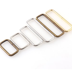 May include: Five metal rectangular rings in different sizes. The rings are in shades of gold, silver, and bronze.