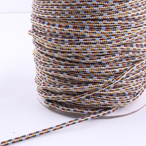 Op de afbeelding: Een spoel met veelkleurige koord met een blauw, geel, rood en bruin patroon. Het koord is strak om de spoel gewikkeld.