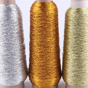 May include: Three spools of metallic thread in silver, gold, and a lighter gold colour. The thread is wound tightly on the spools.