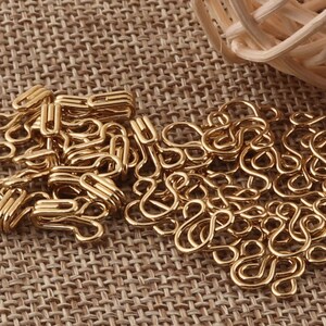 May include: A pile of gold-colored metal hooks, also known as D-rings, on a brown woven fabric background.