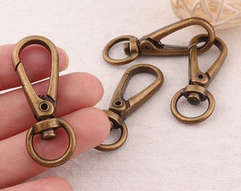May include: Four antique gold-toned metal swivel clasps with a spring-loaded gate. The clasps are ideal for attaching to bags, keychains, or other accessories.