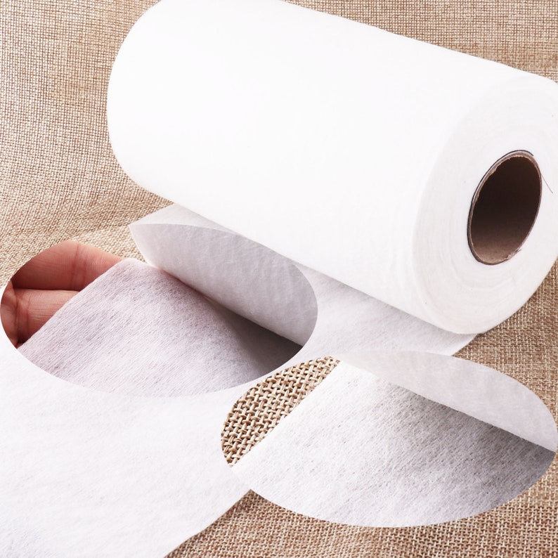 May include: A roll of white non-woven fabric, unfurling to reveal the soft, textured material. The fabric is ideal for crafting, sewing, and other DIY projects.
