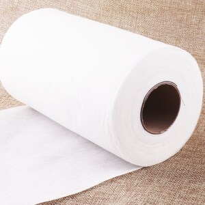 May include: A white roll of non-woven fabric, likely used for crafts or cleaning, is shown on a brown burlap surface.