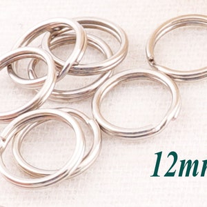 May include: A close-up of a pile of silver key rings, each measuring 12mm in diameter. The rings are arranged in a random pattern on a white surface.