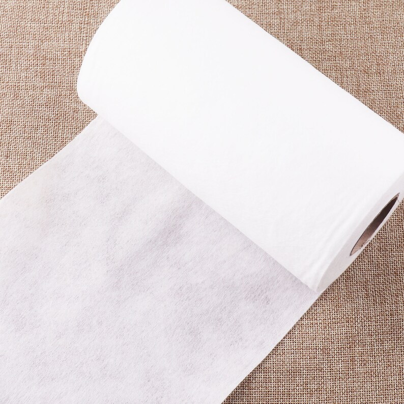 May include: A roll of white non-woven fabric, unrolled on a brown burlap surface.