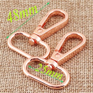 May include: Two rose gold swivel clasps. Each clasp has a textured rectangular hook and an oval ring. The clasps measure 48mm in length and the oval rings measure 25mm.