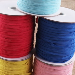 Può includere: Cinque bobine di cordoncino elastico in diversi colori: rosso, blu, giallo, azzurro e rosa. Le bobine sono impilate l'una sull'altra.