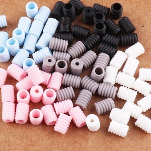May include: A collection of small, cylindrical beads in various colors, including light blue, pink, gray, black, and white. The beads have a ridged, spiral design and a hole through the center, suitable for jewelry making or crafts.