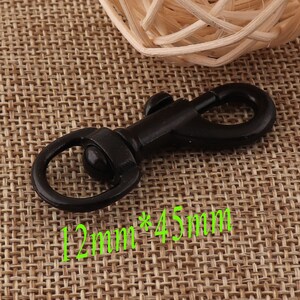 May include: A black metal swivel clasp with a spring-loaded gate. The clasp has a circular ring on one end and a hook on the other. The text "12mm * 45mm" is printed in green. This hardware is suitable for various crafting projects.