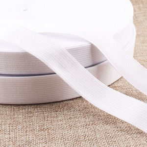 Peut inclure: Bande élastique blanche enroulée sur une surface en tissu brun. La bande élastique est côtelée et a une texture lisse.