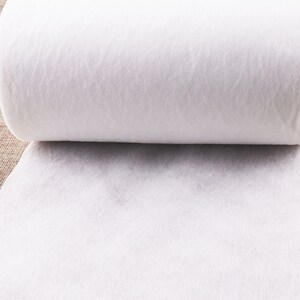 May include: A white roll of interfacing fabric, a type of fusible material used in sewing and quilting projects.