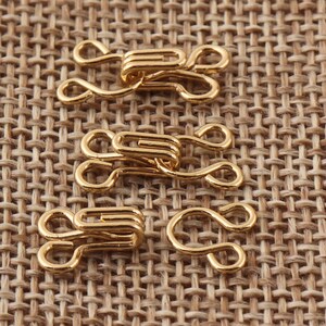 May include: Four gold-toned metal hook and eye closures for sewing projects. The hooks and eyes are in various sizes.