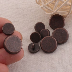 Op de afbeelding: Een set van 10 ronde, antieke bronzen knopen. De knopen zijn glad en hebben een licht getextureerde afwerking.
