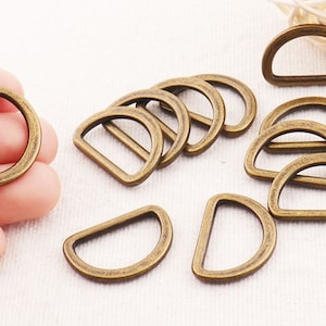 May include: A set of 10 antique gold-toned metal D-rings. The rings are all the same size and shape, and they have a smooth, polished finish.