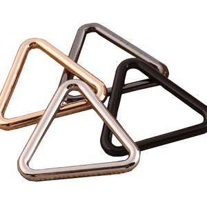 Op de afbeelding: Drie driehoekige metalen ringen in zilver, goud en zwart.
