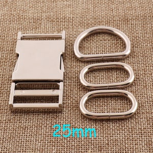 Könnte beinhalten: Silberne Metallschnalle und drei silberne Metall-D-Ringe. Die Schnalle ist 25 mm breit.