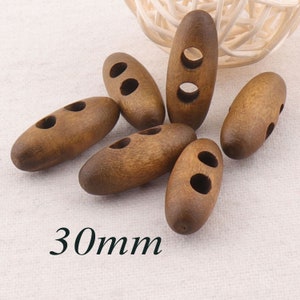Puede incluir: Seis botones de madera marrón con dos agujeros cada uno. Los botones son de forma ovalada y miden 30 mm de largo.