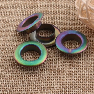 May include: Four iridescent metal grommets with a shiny finish. The grommets are round with a hole in the center.