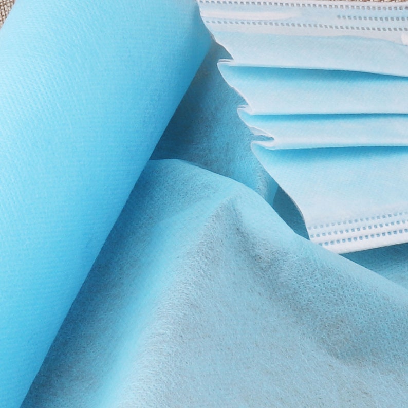 May include: A close-up of a light blue non-woven fabric, commonly used for disposable face masks. The fabric is soft and textured, with a subtle sheen.