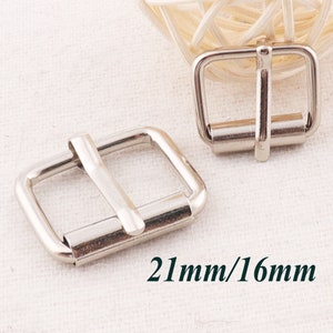 May include: Two silver metal belt buckles, one measuring 21mm by 16mm. The buckles are rectangular with a smooth finish.