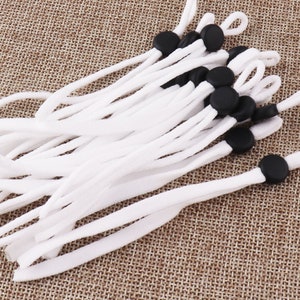 May include: A bundle of white elastic cords with black adjustable toggles. The cords are approximately 50 cm long and are ideal for replacing broken mask ear loops.