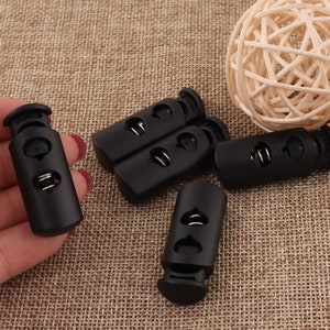 May include: Six black plastic cord locks with a spring mechanism. The cord locks are designed to secure cords or straps.