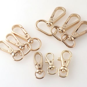 Könnte beinhalten: Ein Satz mit zehn goldfarbenen Schlüsselringen aus Metall mit Drehverschlüssen. Die Schlüsselringe sind in verschiedenen Größen und Formen.