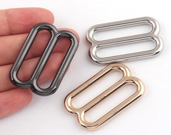 May include: Three metal slider buckles in different finishes: black, silver, and gold. Each buckle has two parallel loops.