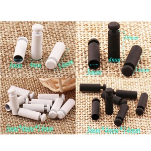 May include: A set of white and black plastic stoppers for clothing. The stoppers are 3mm in diameter, 4mm in diameter, and 14mm in diameter. The stoppers are shown on a woven fabric background.