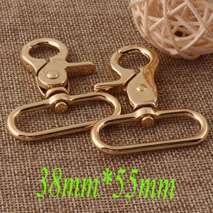 May include: Two gold-colored swivel clasps with a lobster claw design. Each clasp has a rectangular loop and a spring-loaded hook. The clasps are approximately 1.5 inches wide and 2.2 inches long.