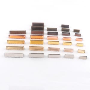 May include: An assortment of rectangular metal bars in various sizes and finishes, including silver, gold, rose gold, and bronze. The bars are arranged on a white surface, showcasing their different colors and textures. These are likely decorative hardware elements.