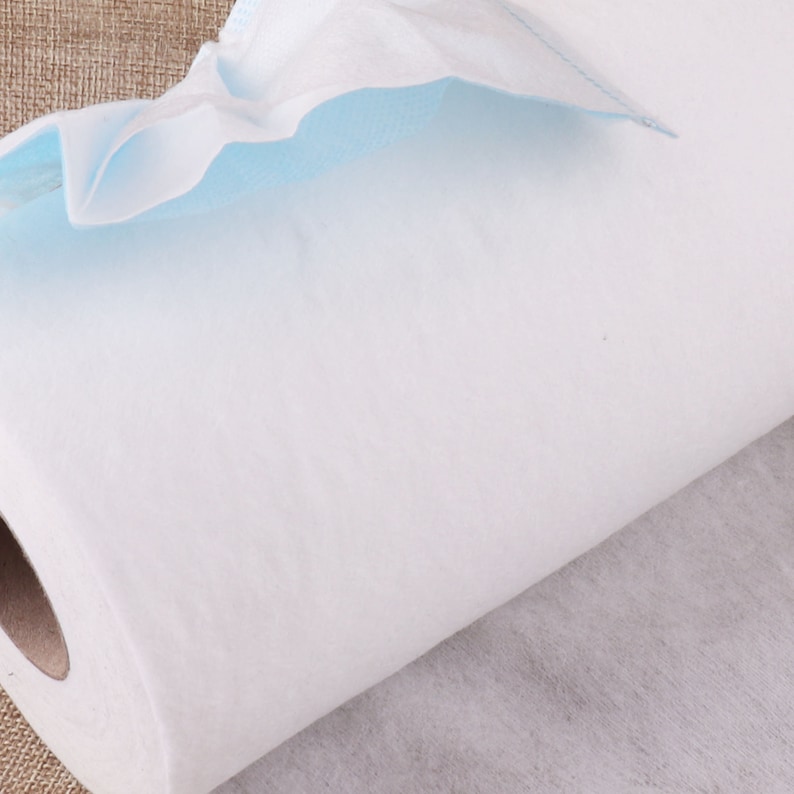 May include: A roll of white non-woven fabric with a blue edge. The fabric is rolled up and the end is visible.