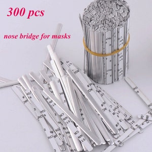 May include: A close-up of 300 silver nose bridge wires for masks. The wires are bundled together and labeled with numbers and letters.