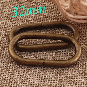 May include: Two antique gold-toned metal oval rings, each measuring 32mm in diameter. The rings are stacked on top of each other, with the top ring slightly offset from the bottom ring. The rings are on a woven fabric background.