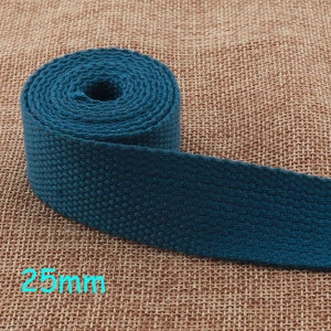 Puede incluir: Primer plano de una correa de cinta de algodón azul turquesa de 25 mm de ancho, enrollada sobre un fondo de arpillera.