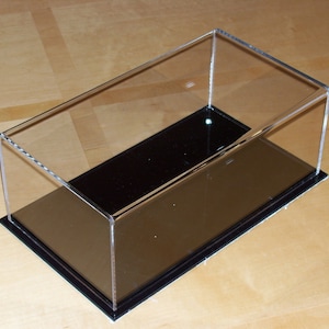 May include: Clear acrylic display case with a black base. The case is empty and ready to display a collectible item.