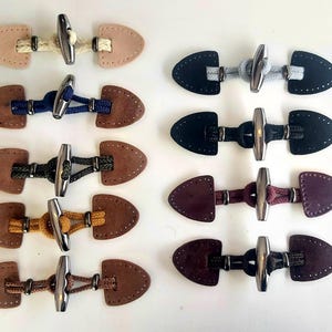 May include: Nine different styles of leather toggles with metal clasps and cord. The toggles are numbered 1 through 9.