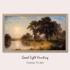 May include: A framed painting of a landscape with a river, trees, and a sun in the sky. The painting is in a light wood frame. The text "Good Light Hunting" is written below the frame.
