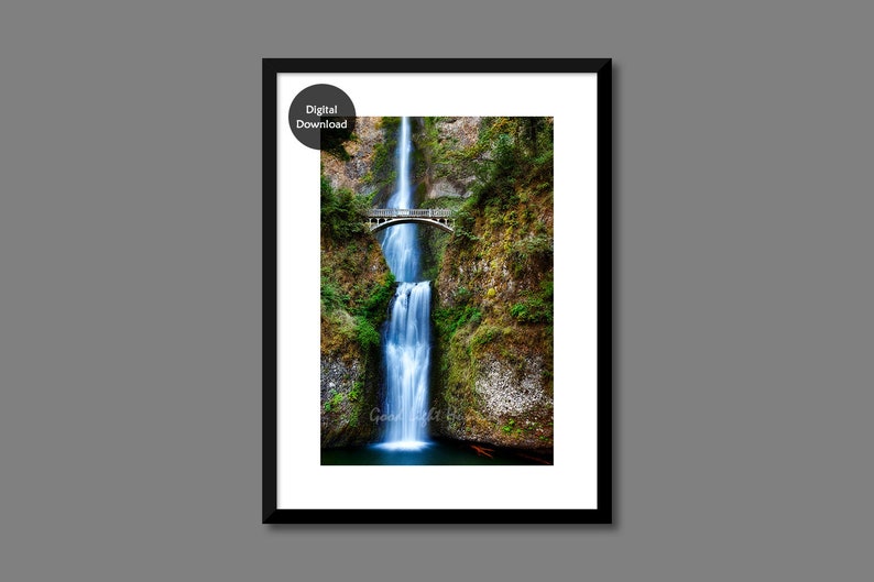 May include: A photograph of a waterfall cascading down a rocky cliff face. A bridge spans the top of the waterfall, with lush green foliage surrounding the area.