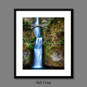 May include: A photograph of a waterfall cascading over a bridge in a lush green forest. The water is a vibrant blue and the bridge is made of wood.